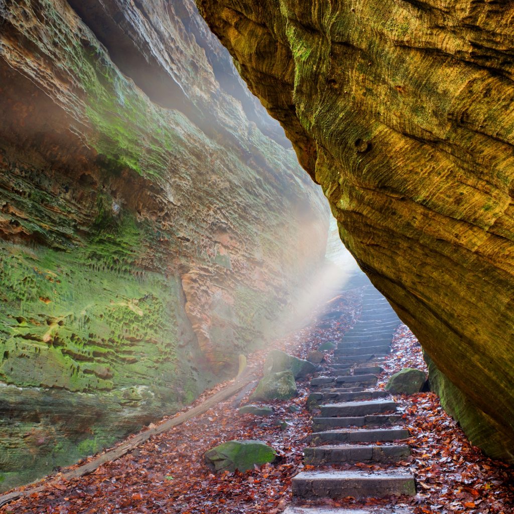 Light streaming through cliffs to a path with stone stairs leading up.